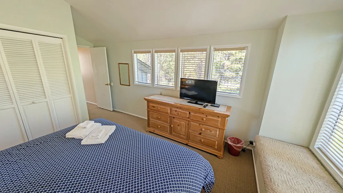 This image shows another king bedroom with blue patterned bedding, a wooden dresser, and large windows that flood the space with natural light. The overall mood is comfortable and cozy, ideal for curling up with a book or unwinding after a day of adventure.