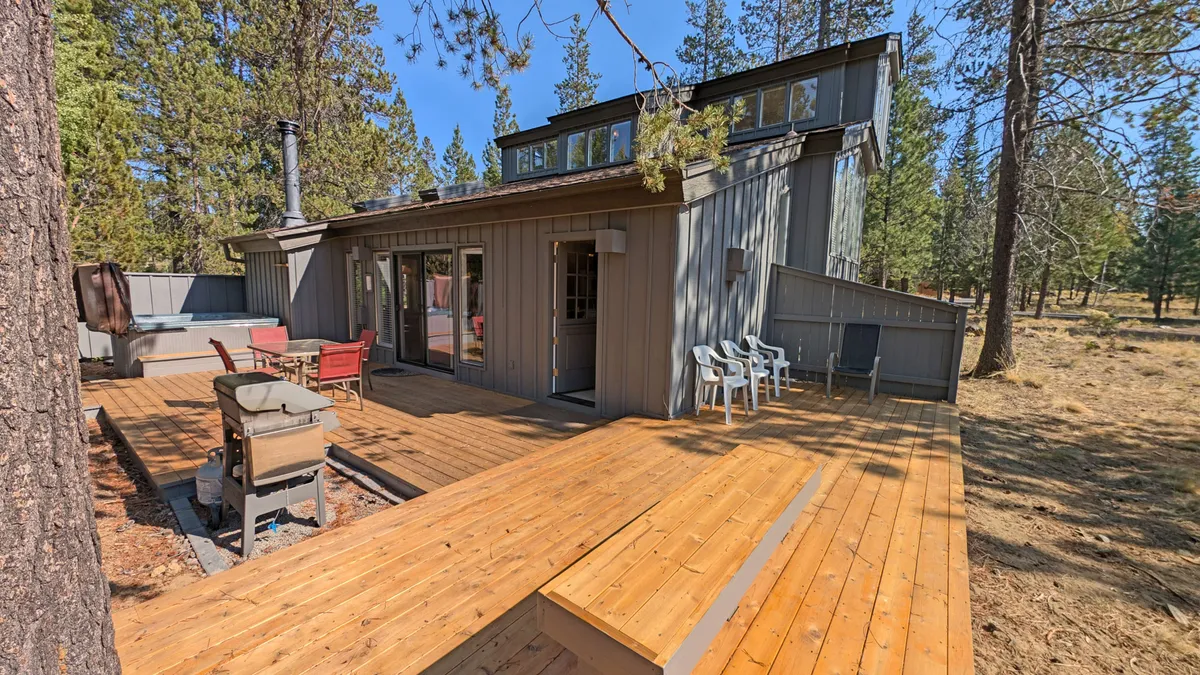 This exterior image displays a wooden deck with outdoor seating and a grill, seamlessly extending the indoor living space. Large windows connect the exterior to the inside, and the setup is ready for outdoor dining or relaxation, capturing the essence of indoor-outdoor living mentioned in the content.