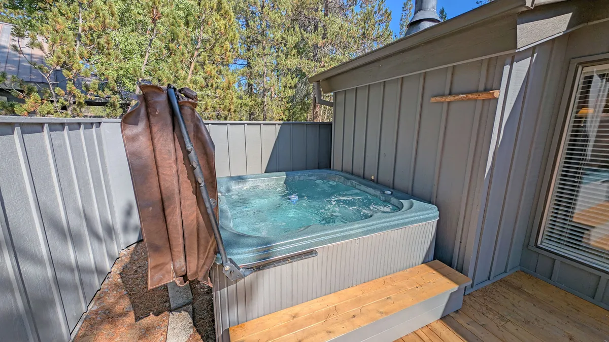 A close-up view of the hot tub on the wooden deck, surrounded by lush trees. The image focuses on the inviting hot tub and the peaceful natural environment, suggesting relaxation and privacy.