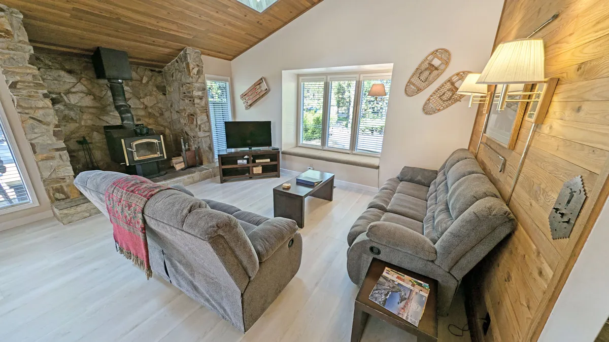 The scene centers around a cozy living room with a prominent stone fireplace, comfortable seating, a TV, and a coffee table. The warm ambiance and inviting furnishings make this an ideal spot for family movie nights or board games by the fire, echoing the text’s description of shared activities.