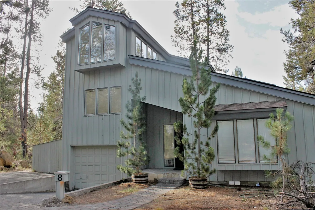 A welcoming exterior shot of the home, highlighting tall windows, an asymmetrical roof, and the surrounding pine trees. The front entrance invites families in from their outdoor adventures, while the natural landscape conveys Sunriver's forested setting.